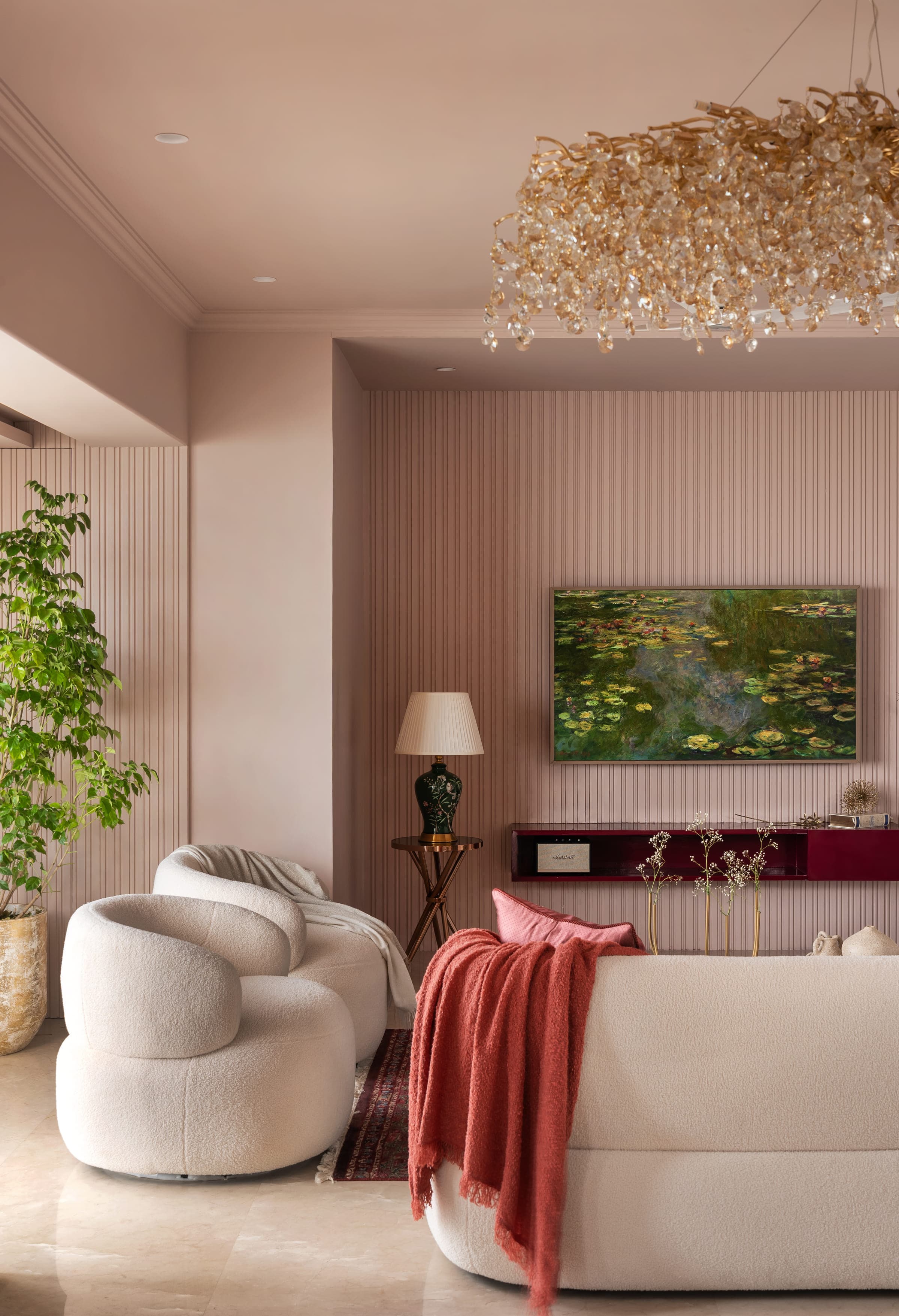 A fluted blush wall at Sea-facing home in Bandra, a lotus painting above a low burgundy lacquered console and a tall plant beside it.